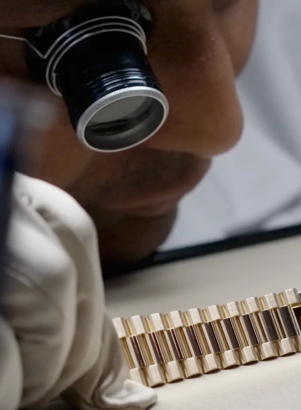 Certified watch repairer inspecting a gold Rolex bracelet through a loupe